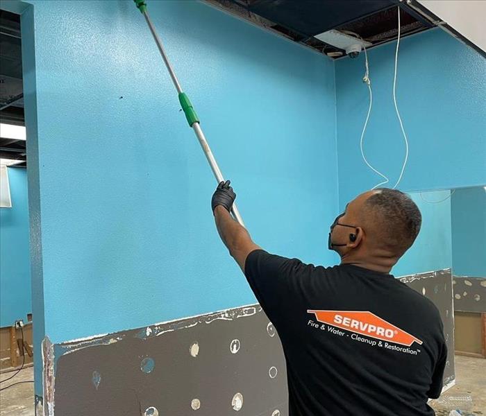 SERVPRO tech cleaning a wall with an extended manual cleaning instrument near an exposed ceiling