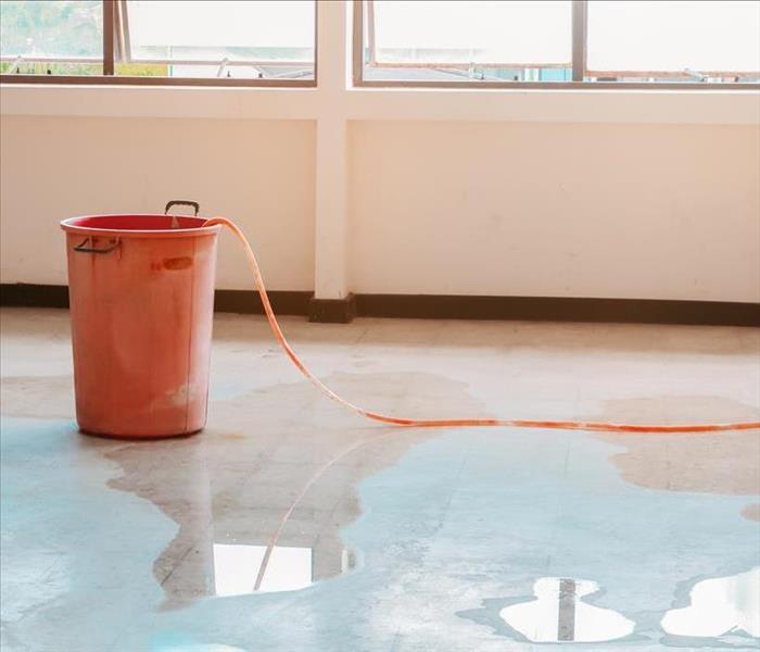 A red bucket and hose on saturated wet floor with water damage.