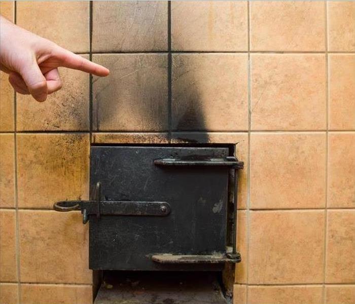 Hand pointing to the soot marks from furnace on tiles wall.